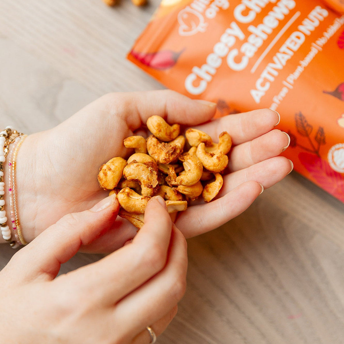 Hand holding cheesy cashews with a package of Cheesy Cashews in the background
