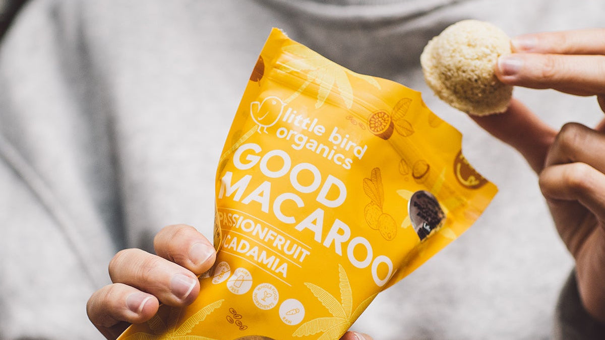 Person holding a yellow package of 'Good Macaroon' snack with a close-up of a macaroon.