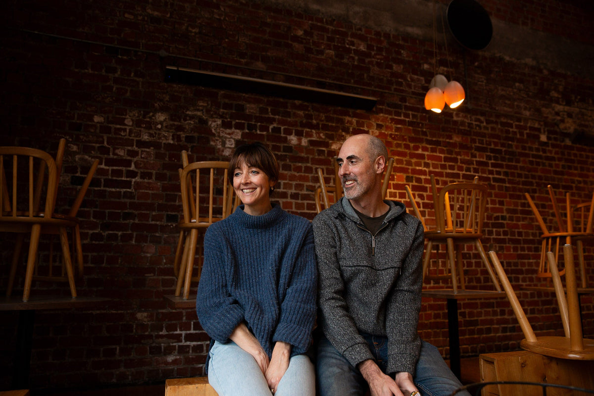 Man and woman sitting together in a cozy room with wooden chairs and a brick wall.