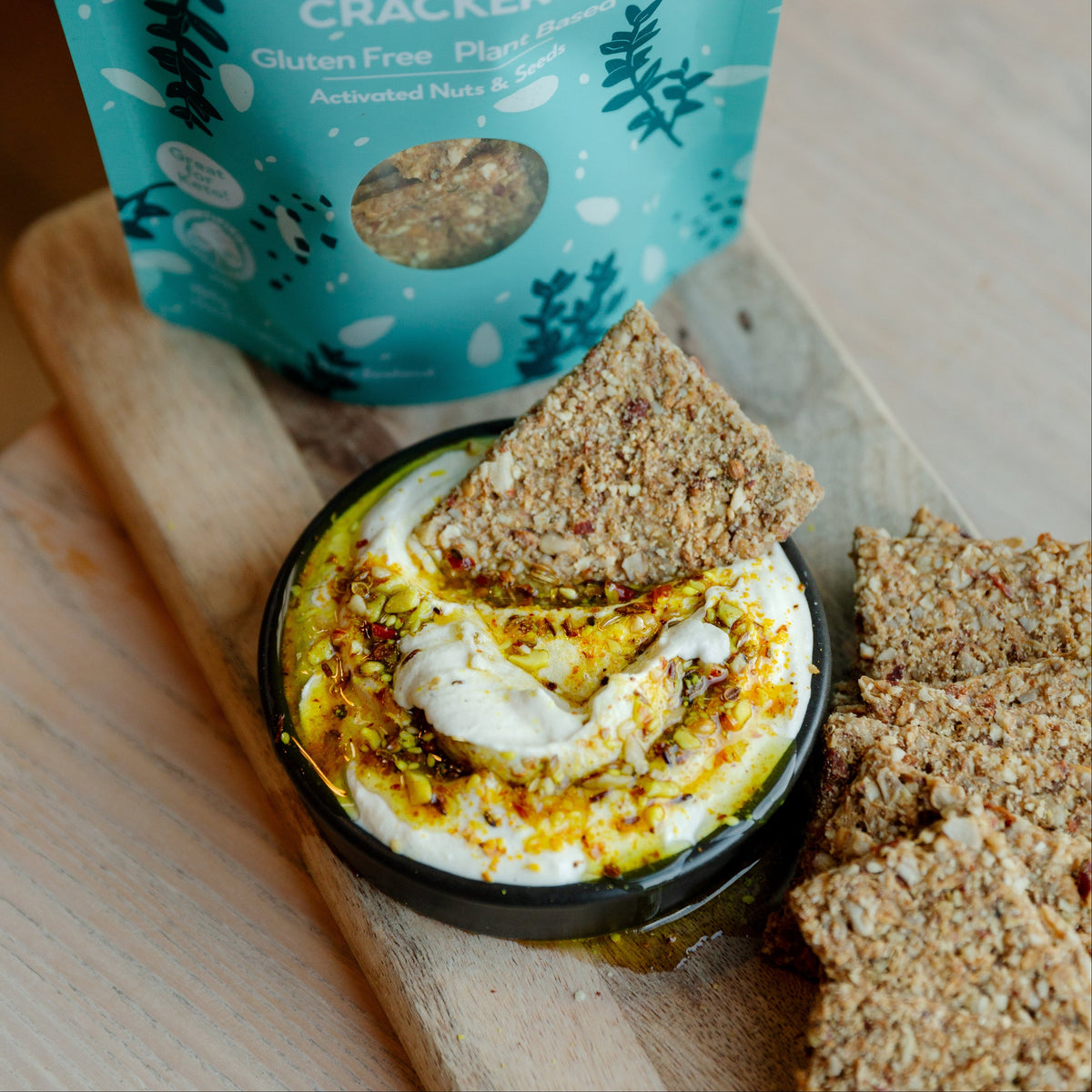 Activated crackers with a dip on a wooden board, next to a package of Little Bird Organics Sea Salt & Thyme crackers.